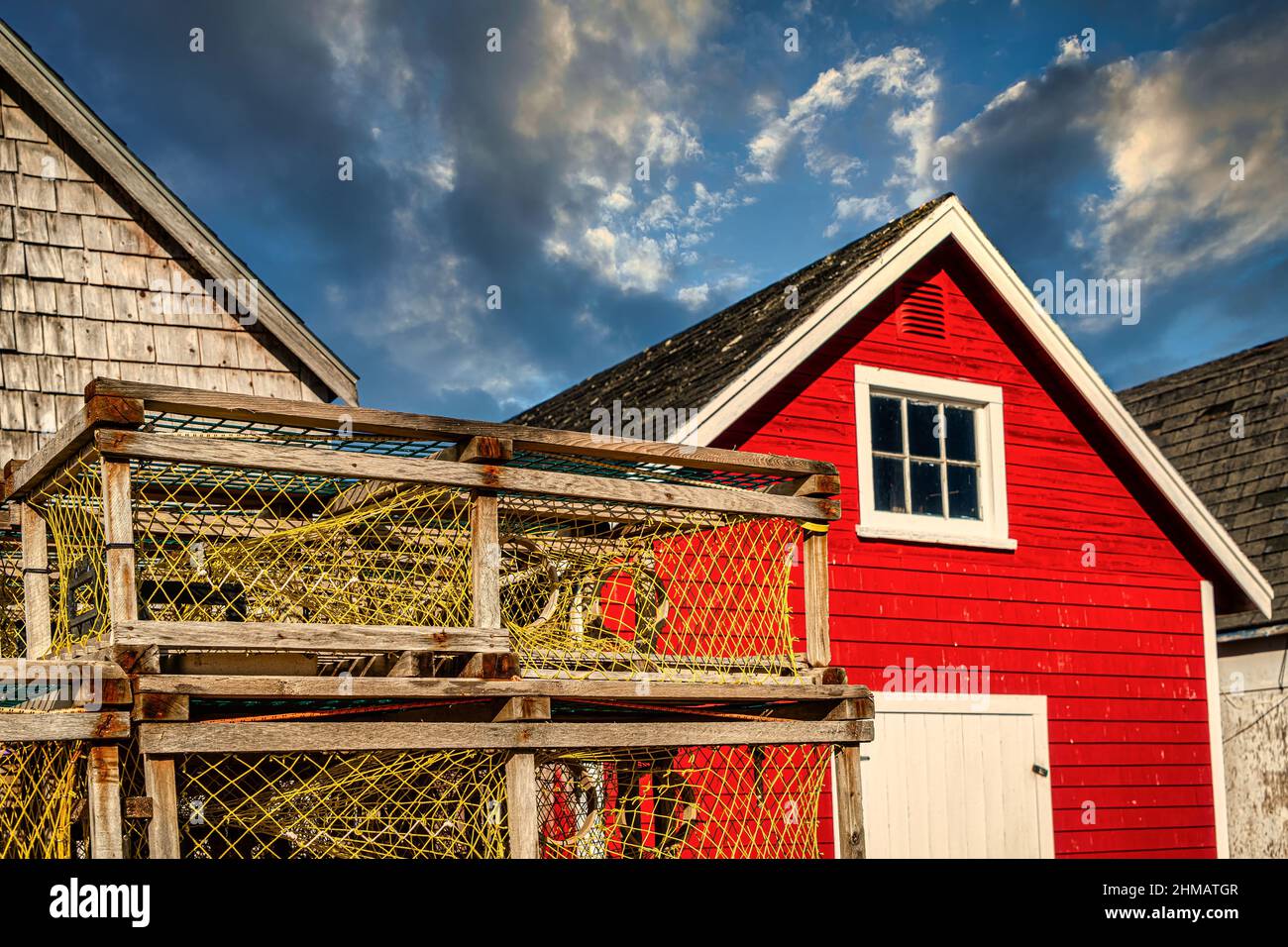 Lobster traps piled up on a wharf in front of colorful bait sheds Stock