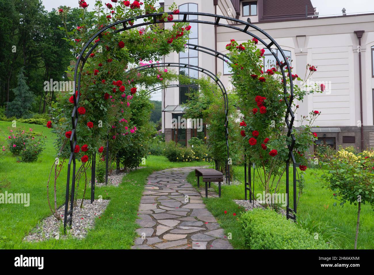Landscape design. Trees, bushes, green lawns. Flower arch with red roses. Beautiful park near the green forest Stock Photo