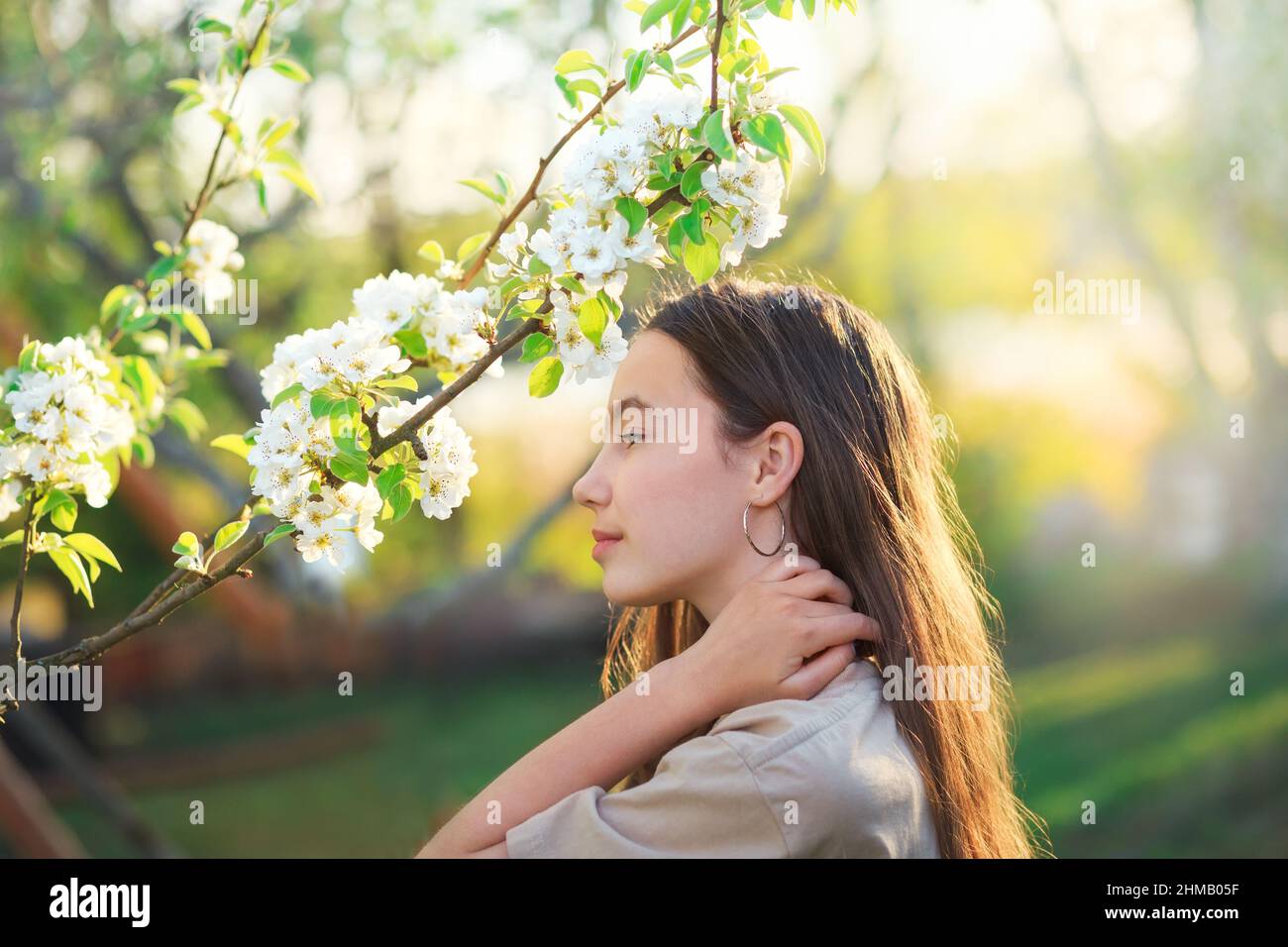Beautiful teen girl with blooming apple flowers. Happy cute kid having fun outdoors at sunset. Stock Photo