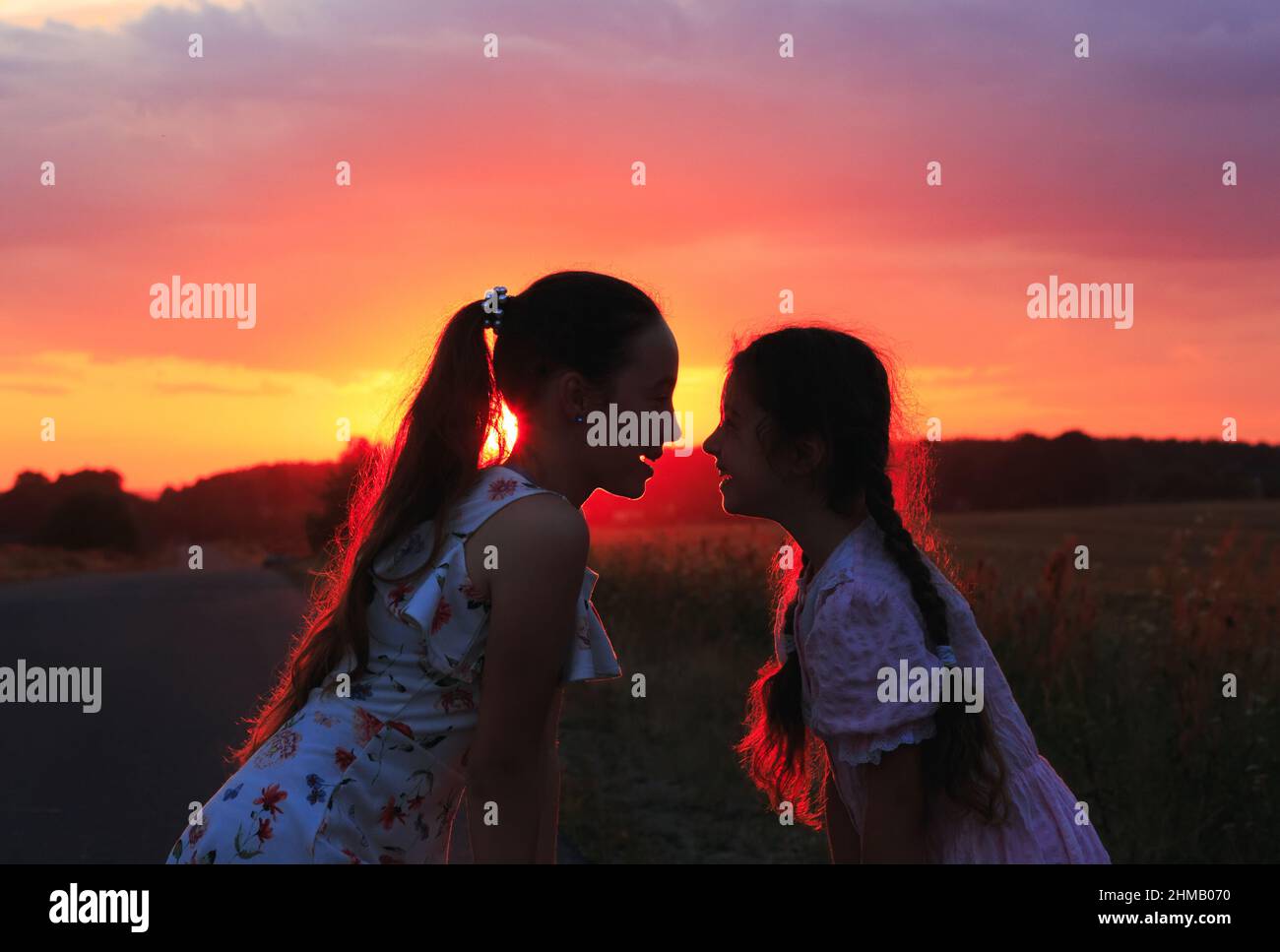 Silhouette of two little girls smiling on sunset. Sisters enjoyed a Holiday over blurred summer nature. Hhappy childhood concept. Stock Photo