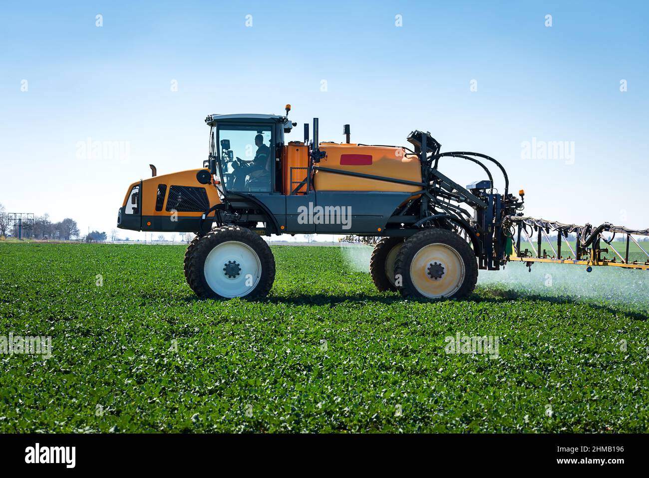 Aerial image of tractor spraying soil and young crop in springtime in field. Stock Photo