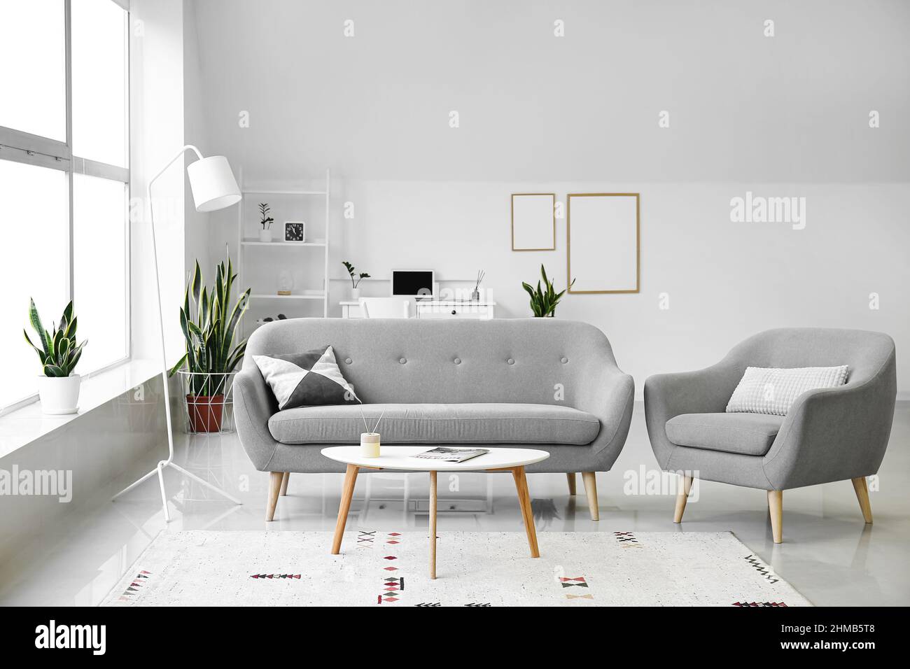 Interior of light living room with grey sofa, armchair and table Stock