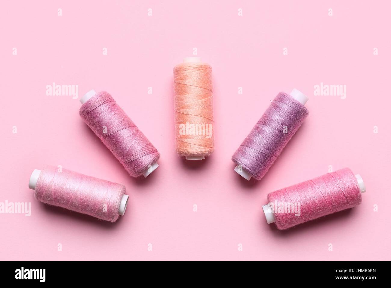 Different sewing threads on pink background Stock Photo - Alamy