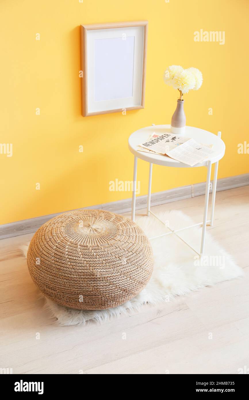 Table with flowers in vase and pouf near yellow wall Stock Photo