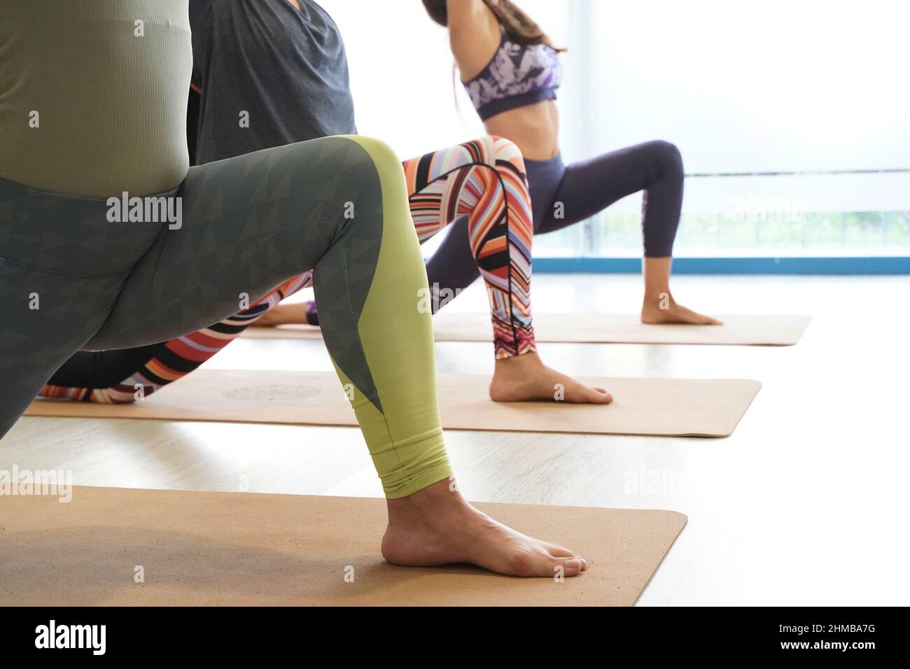 close-up of the legs of three beautiful Caucasian women with slim bodies doing yoga in yoga class, preparing for the yoga posture virabhadrasana. Stock Photo