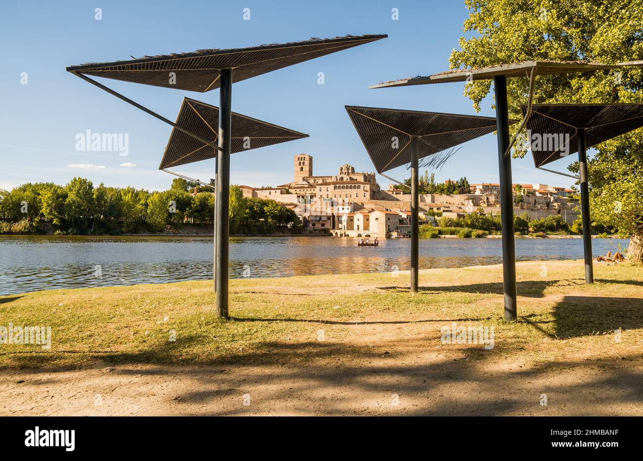 View of the cathedral with the mills and the Duero river where there is a barge crossing the water with tourists during a sunny summer day in Zamora, Stock Photo