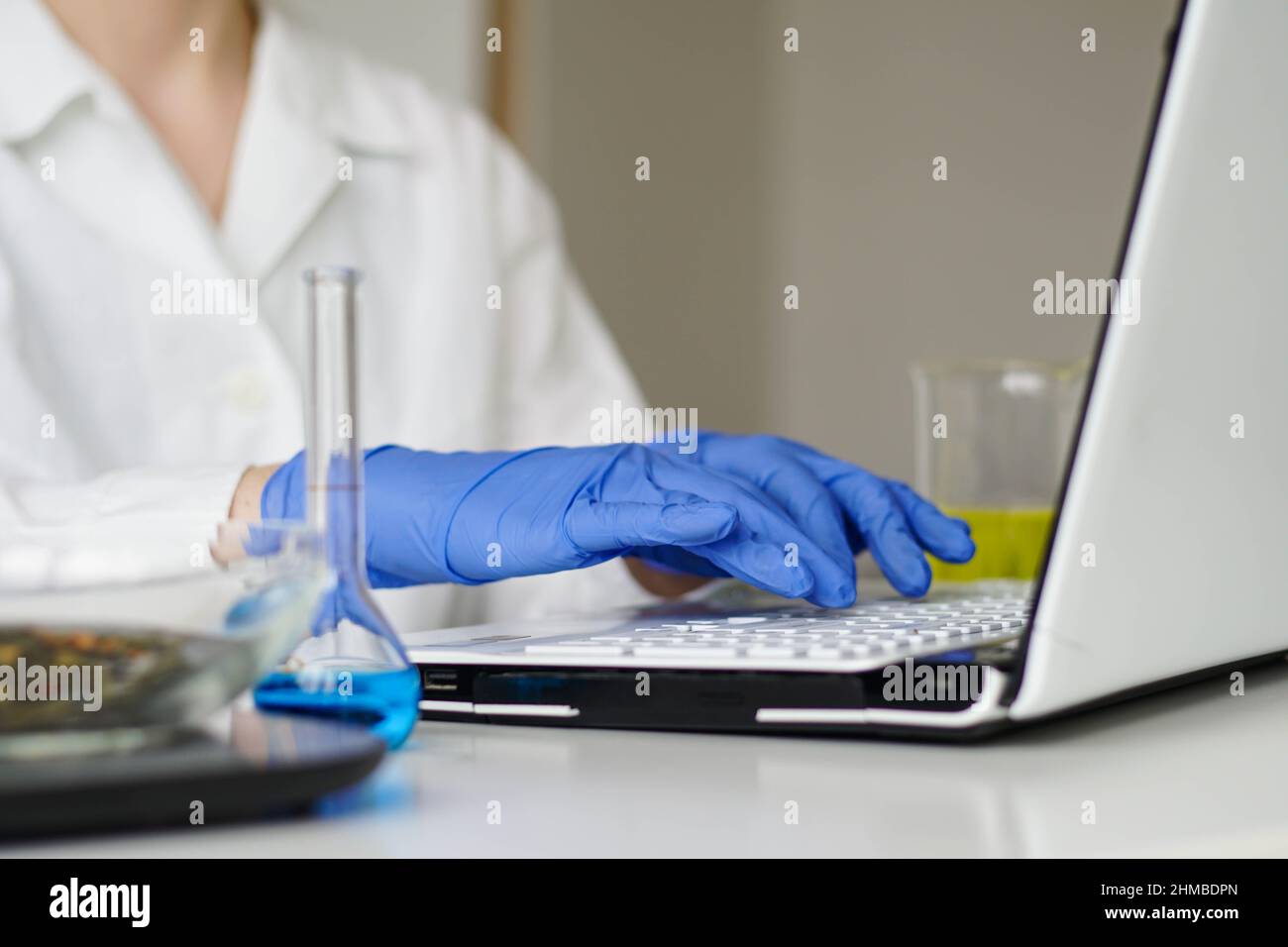 Female scientist in white coat typing on laptop computer keyboard in laboratory. Online medical working. Stock Photo