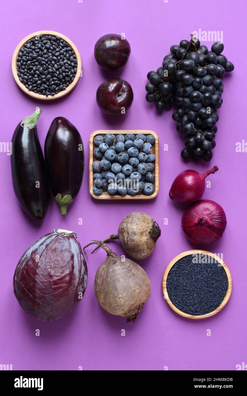 Dark purple and black fruits and vegetables on a purple background. Beans, eggplants, cabbage, beets, blueberries, plums, grapes, onions, black sesame Stock Photo