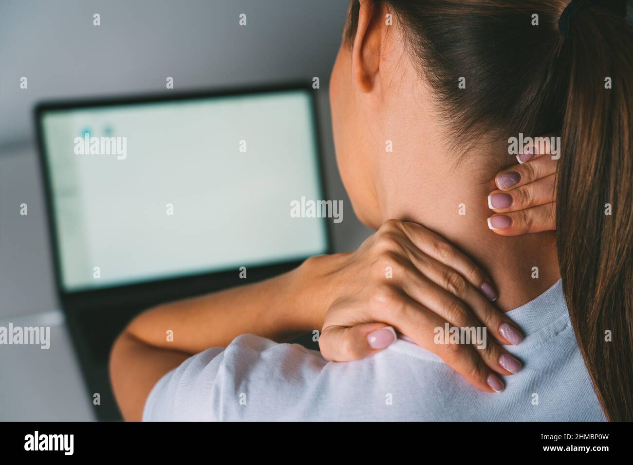 Neck pain after working on laptop or computer. Young woman massaging neck to relieve pain after working on pc Stock Photo