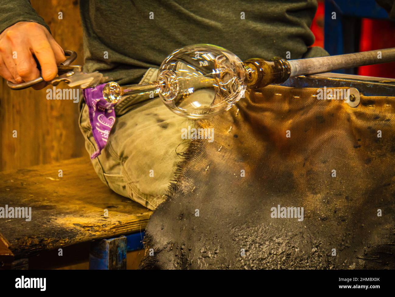 glass blower shaping a glass goblet on his lap while hot Stock Photo