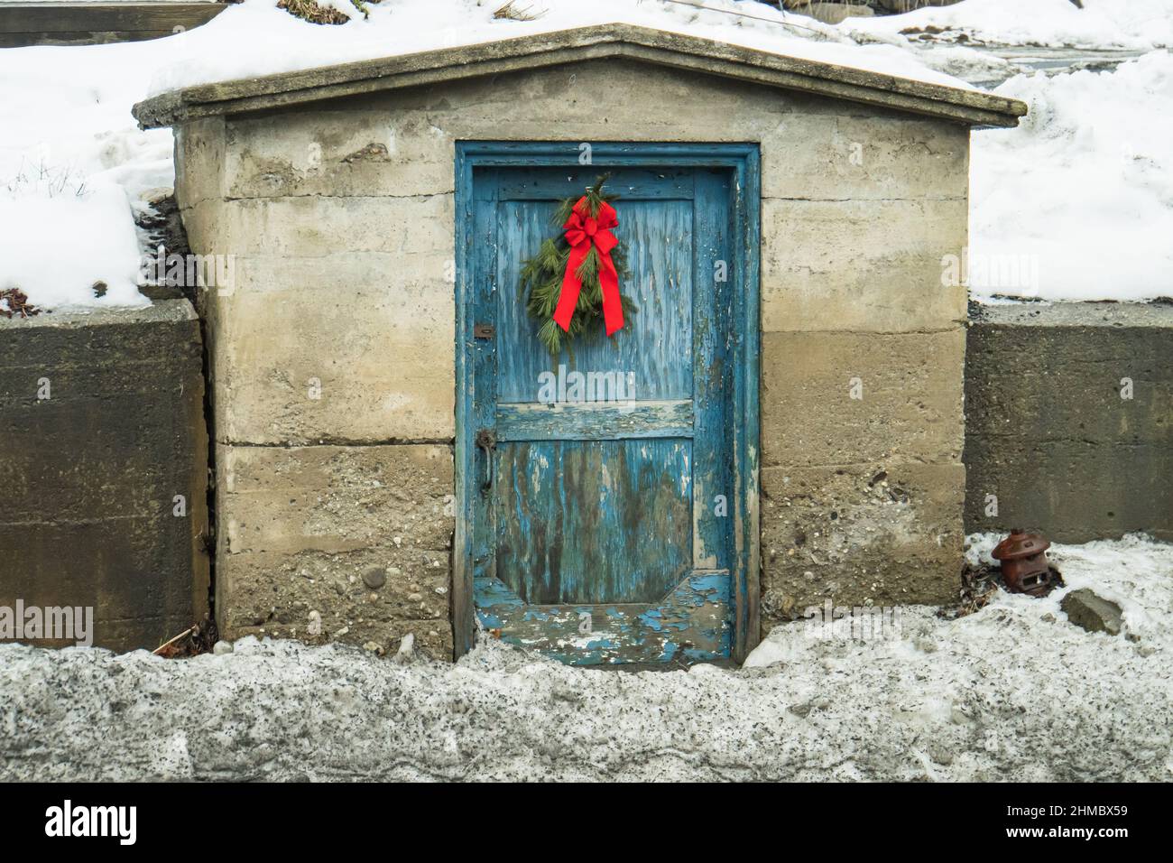 a town shed with peeling blue painted door and a holiday evergreen bough with a red bow Stock Photo