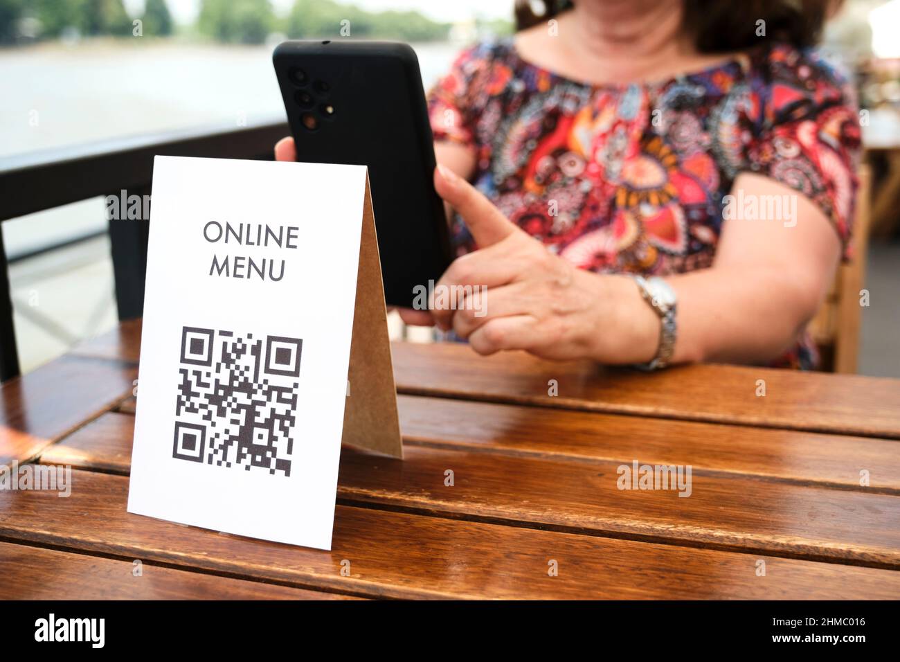 Mature unrecognizable woman scanning a QR code to access a restaurant menu; use of contactless technology in everyday life. Stock Photo