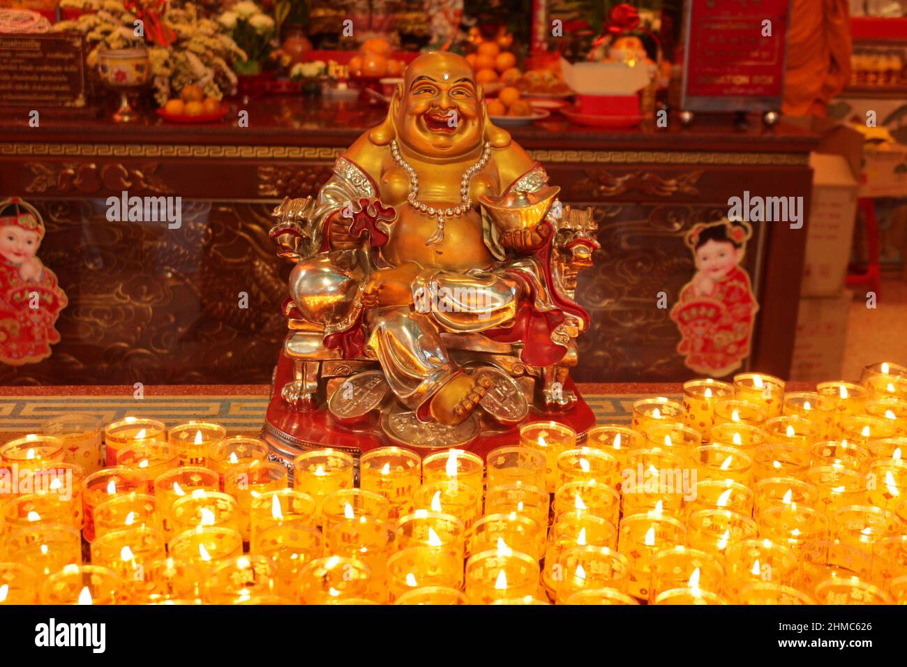 Smiling Golden Buddha Statue, Chinese God of Happiness with candles as offerings in foreground, Chinatown, Bangkok,Thailand Stock Photo