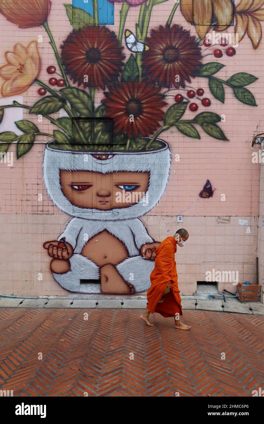 Buddhist Monk walking past  a painting by Thai artist Alex Face featuring his famous character Mardi; Klong Ong Ang Walking Street, Bangkok, Thailand Stock Photo