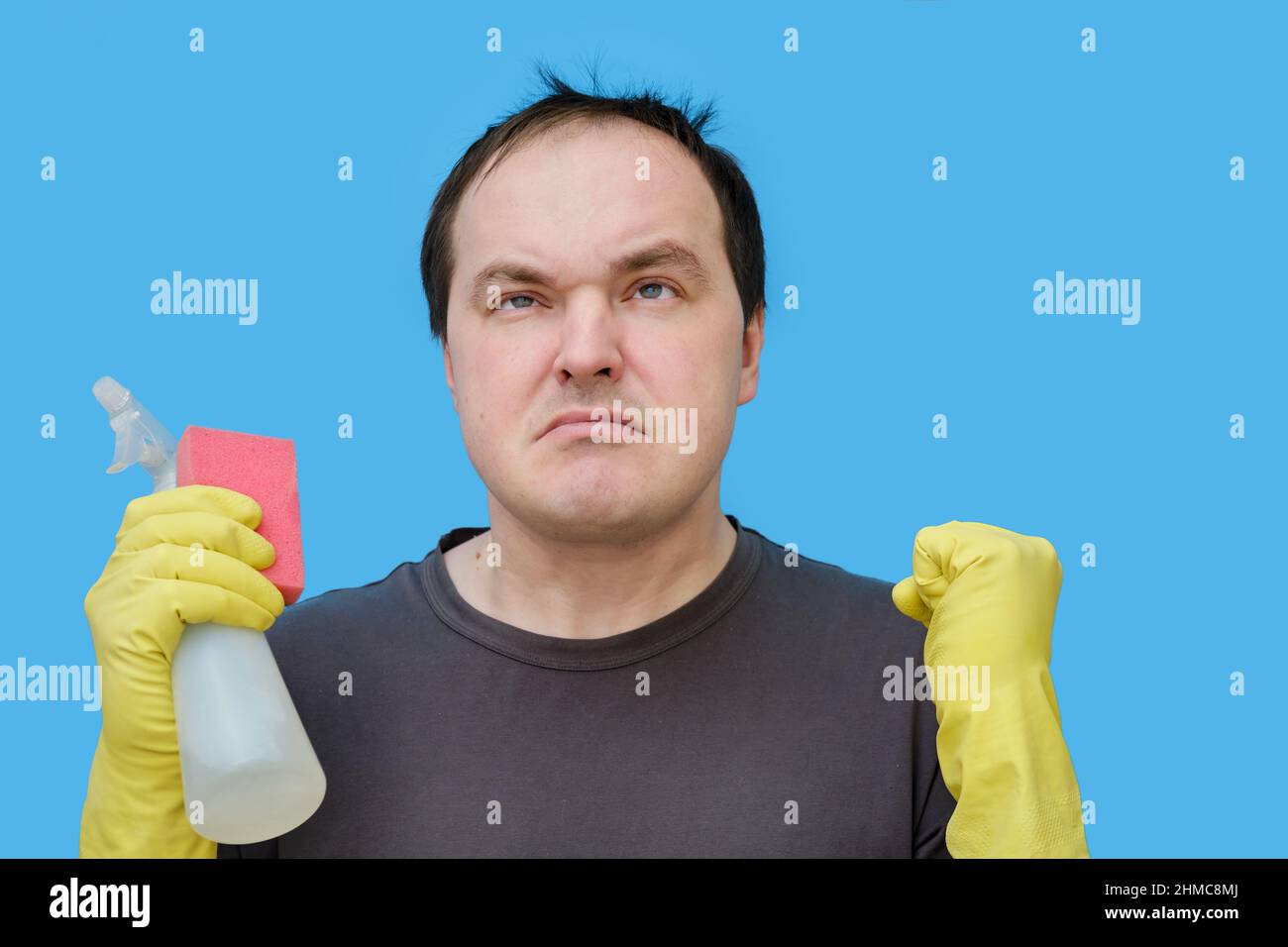 Angry male cleaner in yellow gloves, studio blue background Stock Photo