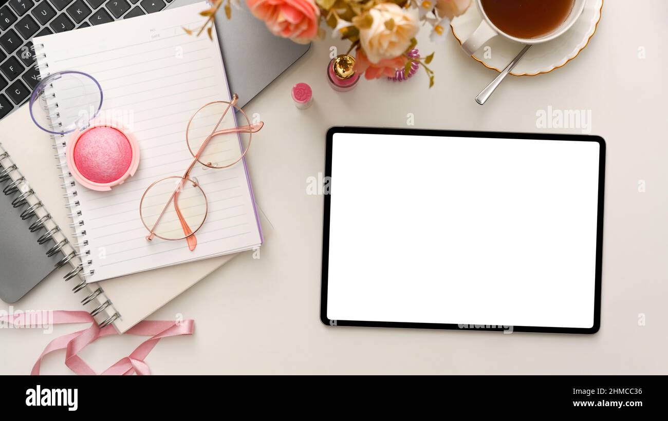 Female beauty blogger workspace with laptop, flowers, teacup, makeups, notebook and digital tablet white screen mockup on white background. top view, Stock Photo