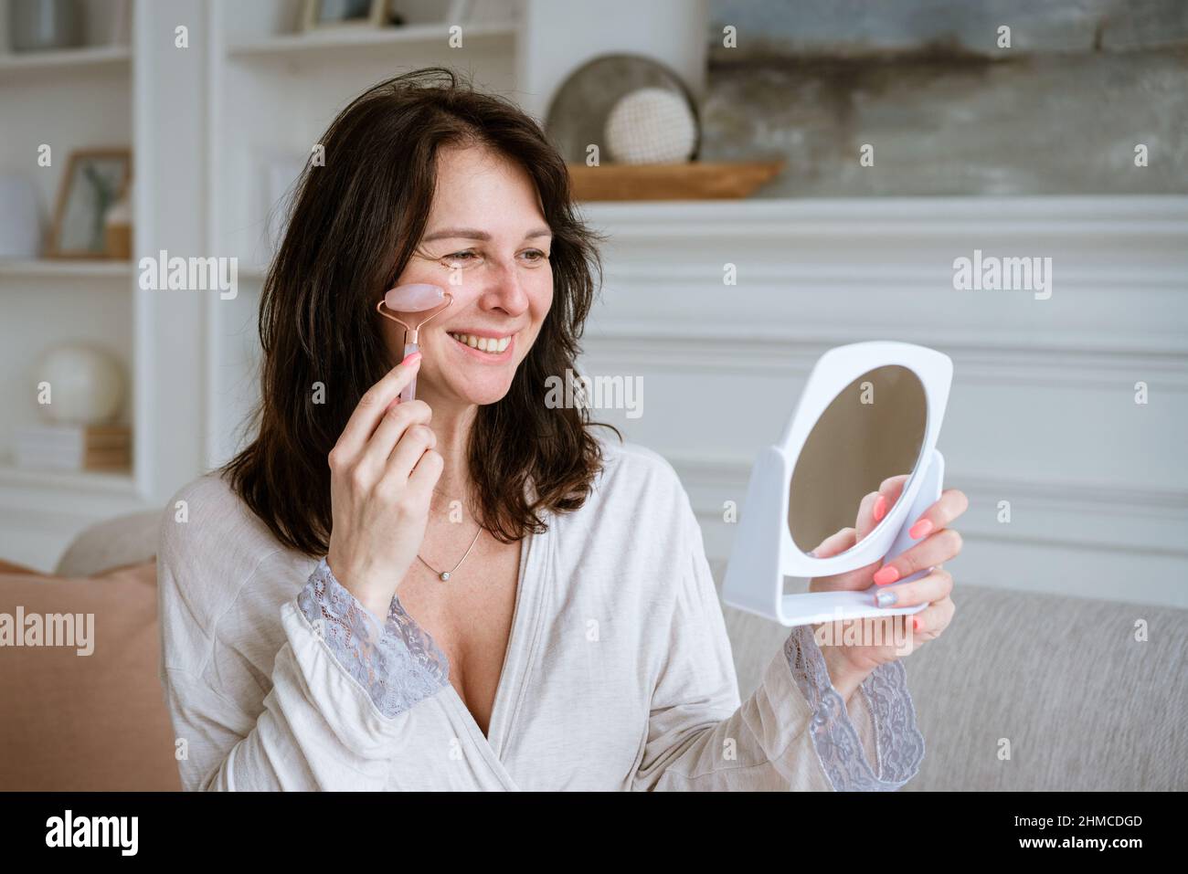 Woman massages her face with pink stone roller, facial massage at home