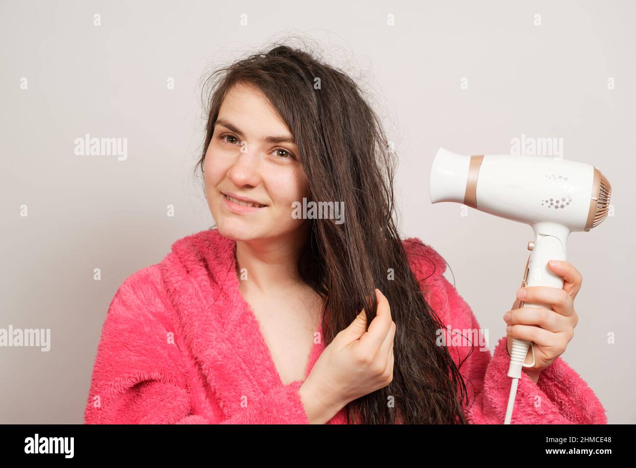 A beautiful happy woman dries her wet hair with a hair dryer and smiles ...