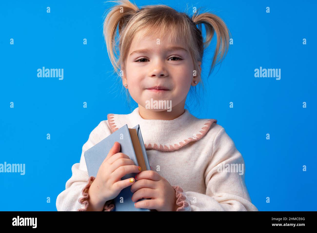Cute little girl with book on blue background Stock Photo - Alamy