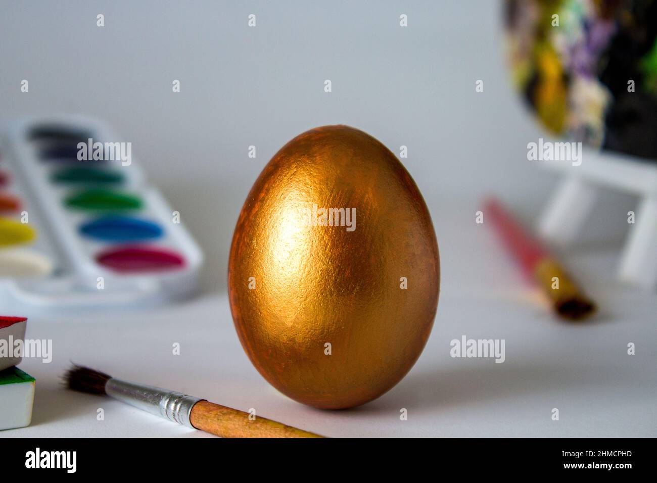 Golden Easter egg on a watercolor background. Simple holiday composition. Symbolism of the Easter egg festival concept. Art work, handmade, creativity Stock Photo