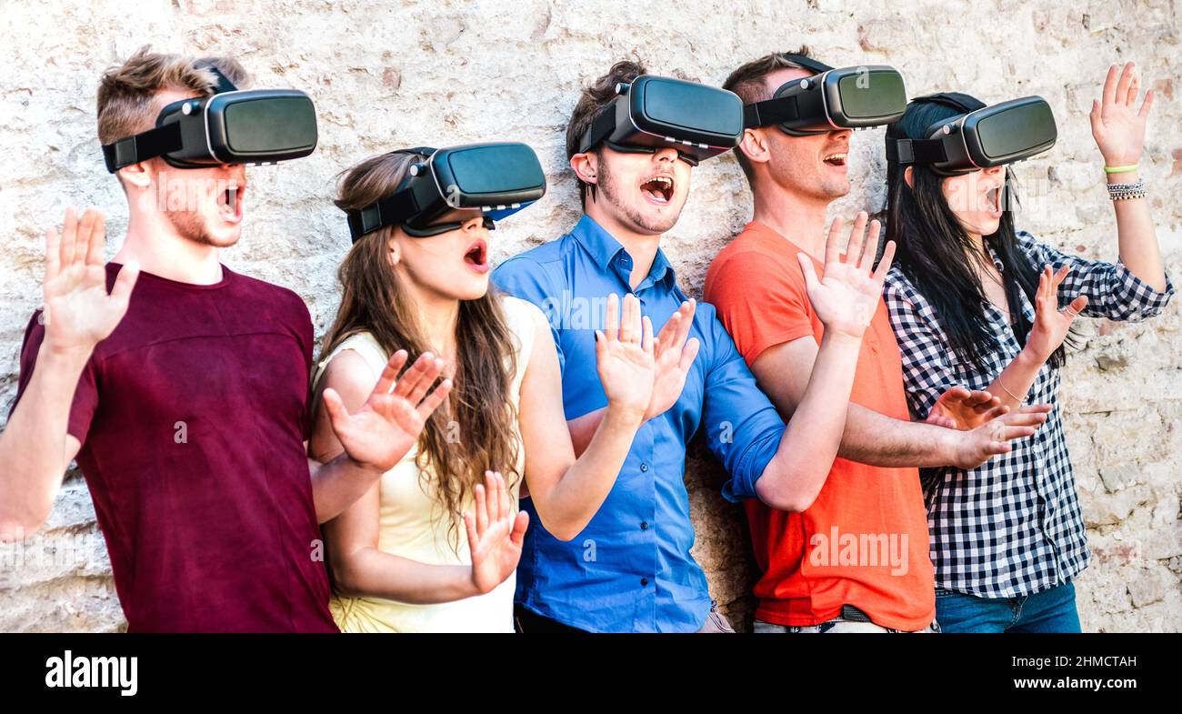Surprised friends exploring metaverse on vr glasses - Virtual reality and wearable tech concept with happy people having fun together with headset gog Stock Photo