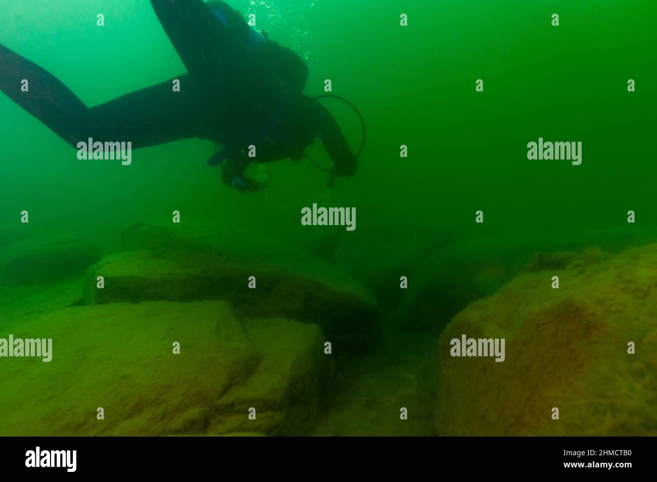 SCUBA diver exploring a cloudy inland lake and boulders with a diving