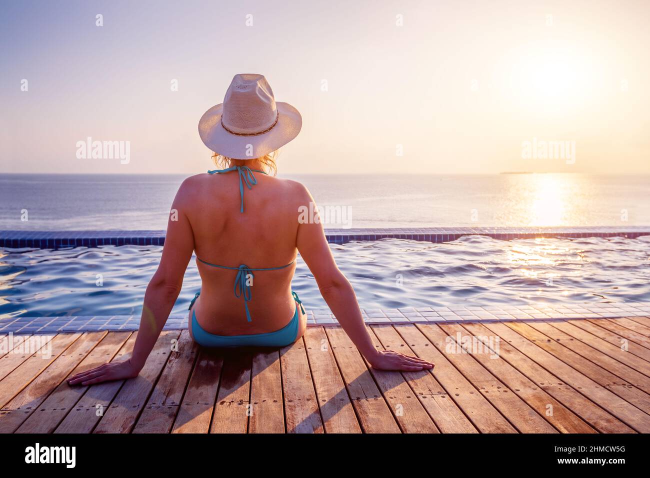 Woman enjoying beach vacation holidays, relaxing at infinity swimming pool of luxury resort hotel, looking at sunset. Warm tropical water, blue sky, s Stock Photo