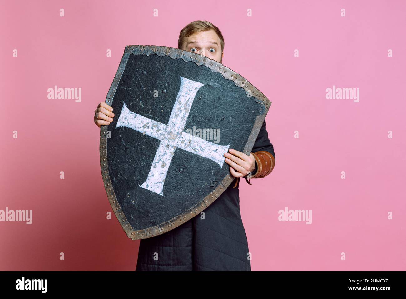 Portrait of surprised man, medieval warrior or archer in armor hiding  himself behind a shield isolated over pink studio background Stock Photo -  Alamy