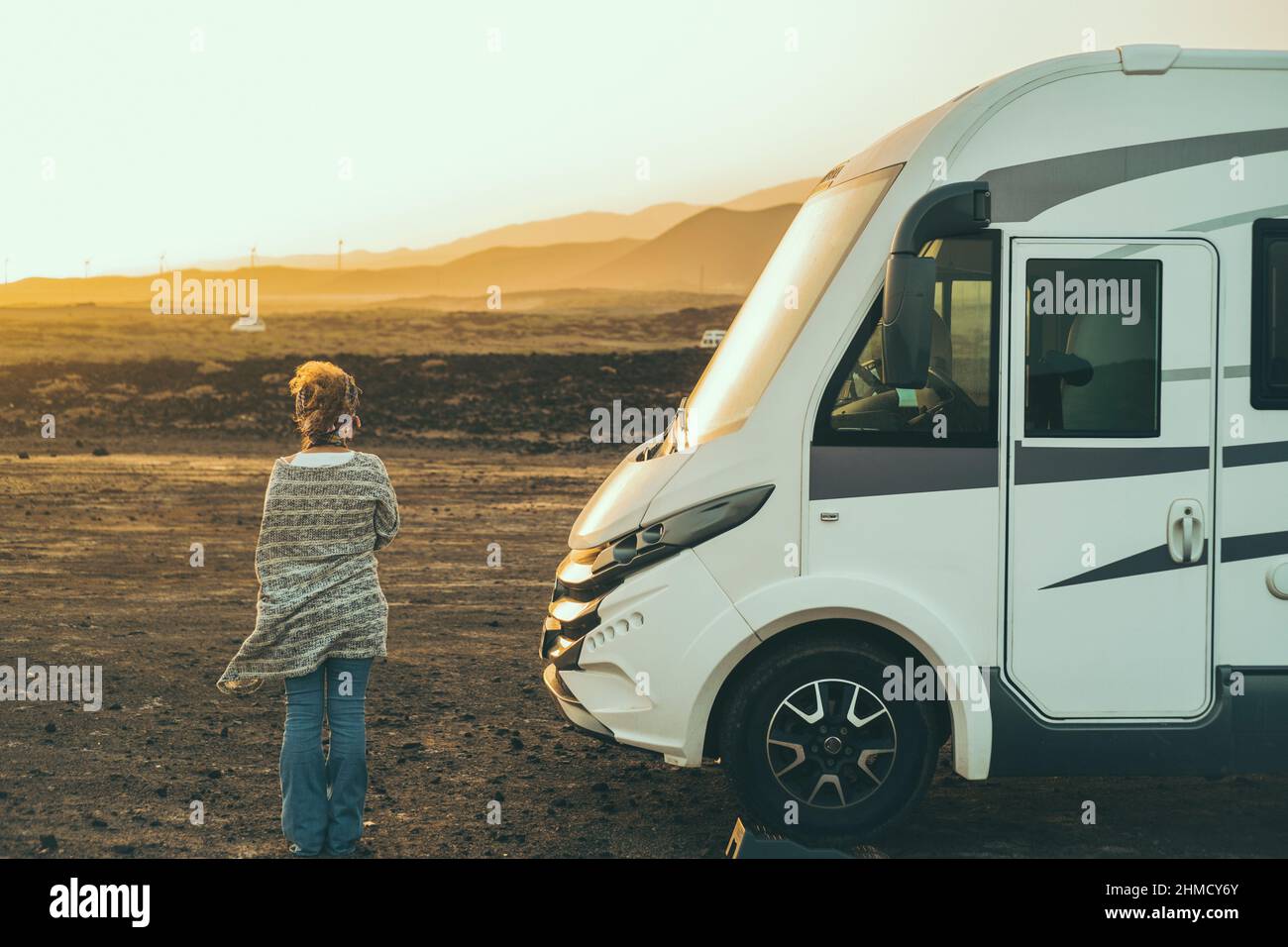 Alternative tourist vanlife concept with standing woman in back view near a big camper van motornohome enjoying the freedom and desert scenic nature p Stock Photo