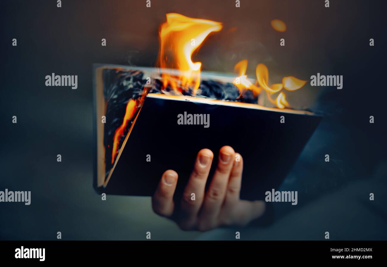 The man holds in his hand a black open book, the pages of which burn with a bright flame and smoke. The Antichrist burns a religious book. Censorship. Stock Photo