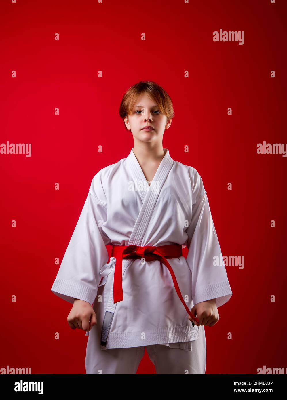 A young girl karateka in a white kimono and a red belt trains and performs a set of exercises on a bright red background Stock Photo