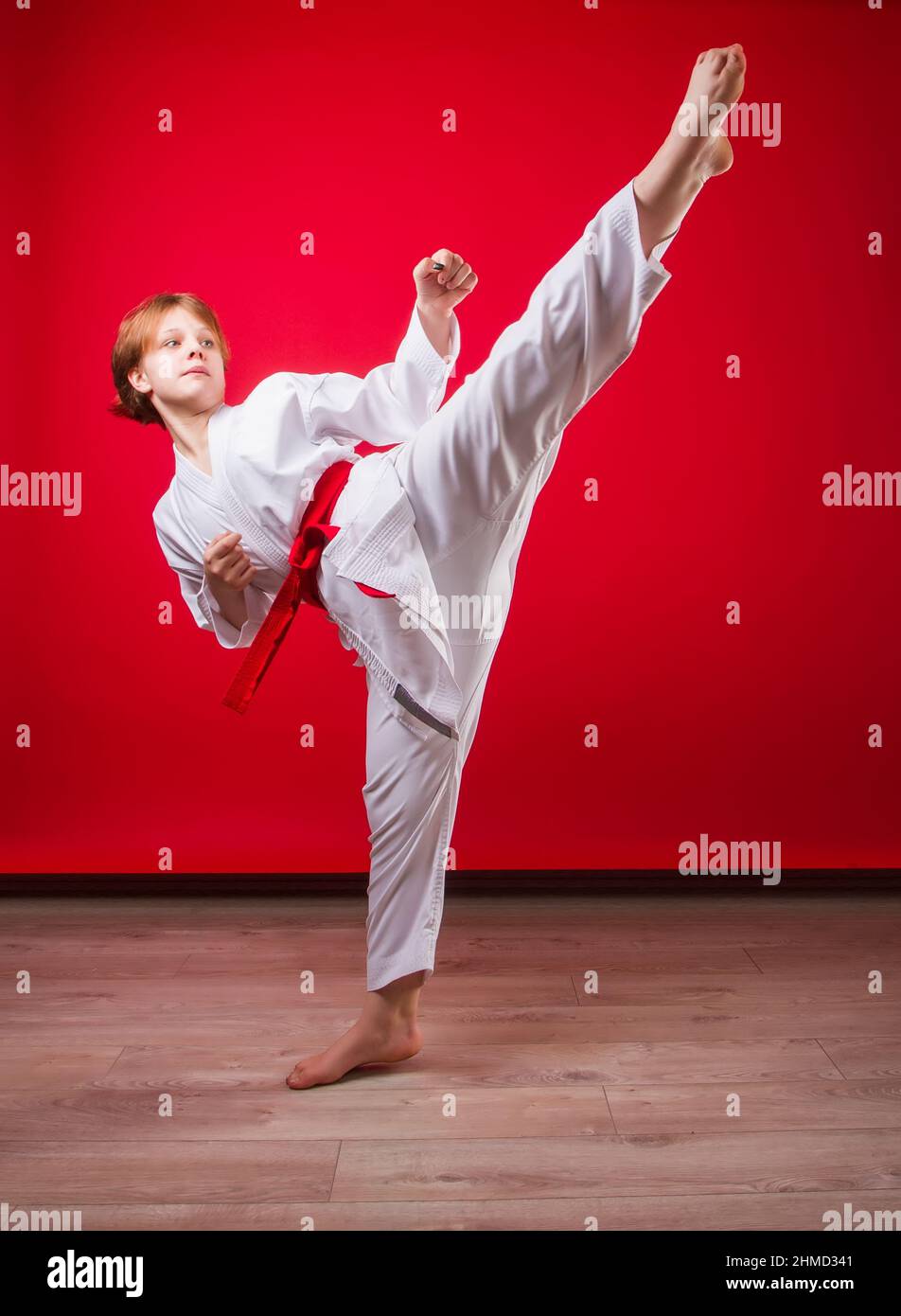 A young girl karateka in a white kimono and a red belt trains and performs a set of exercises on a bright red background Stock Photo