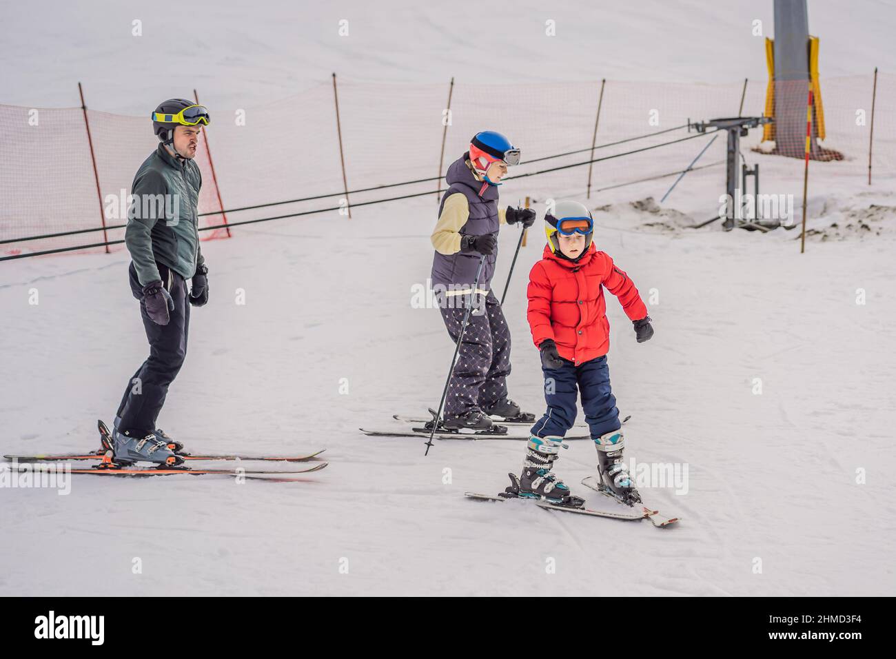 Mom and son are learning to ski with an instructor. Active toddler kid with safety helmet, goggles and poles. Ski race for young children. Winter Stock Photo