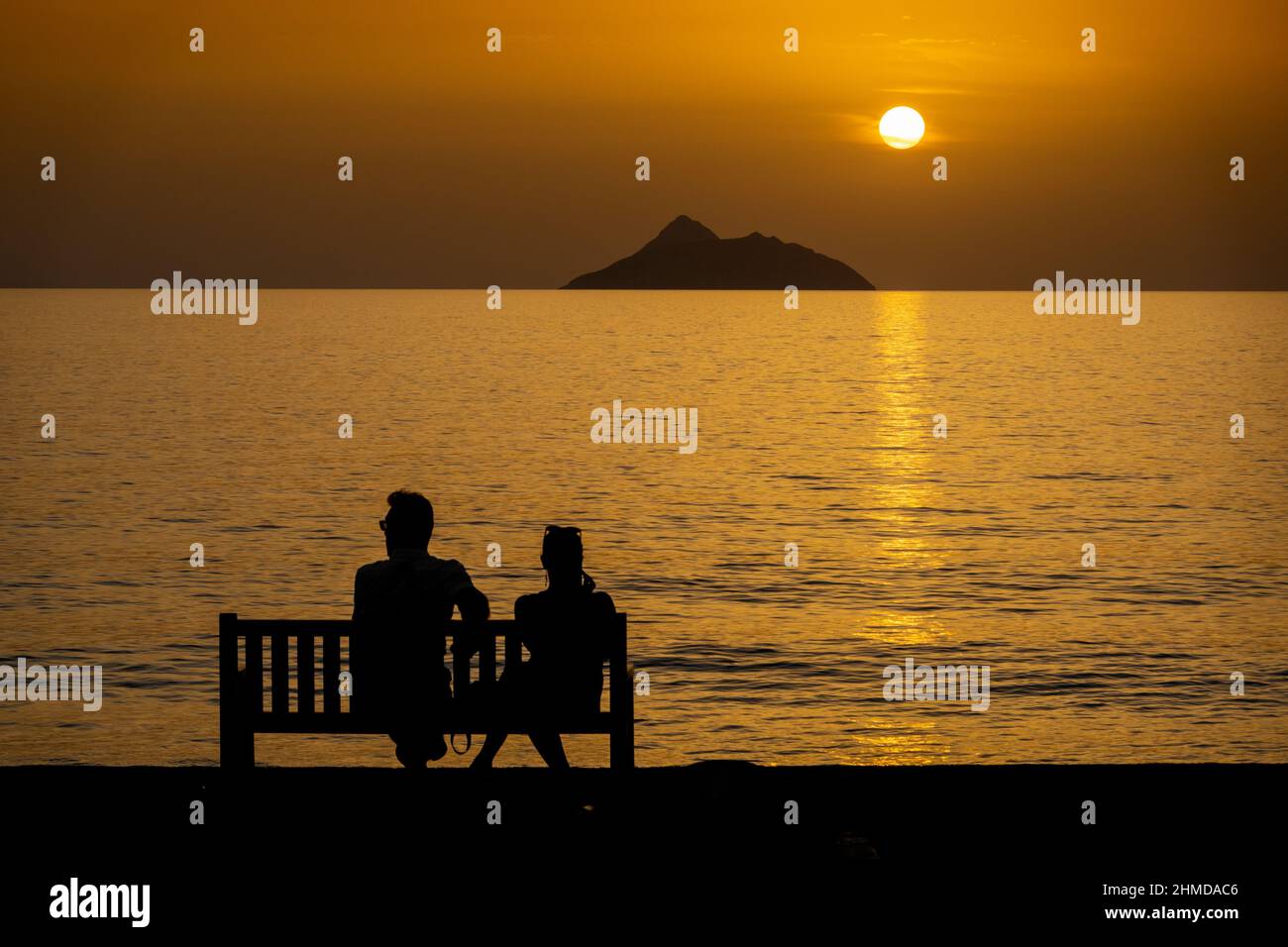 Silhouette of couple relaxing on bench by sea during beautiful sunset Stock Photo