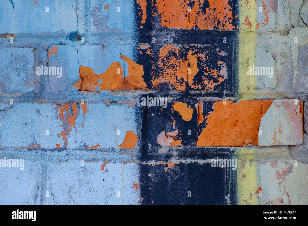 Old colorful orange blue black paint with cracks on red brick wall as background, texture, selective focus Stock Photo