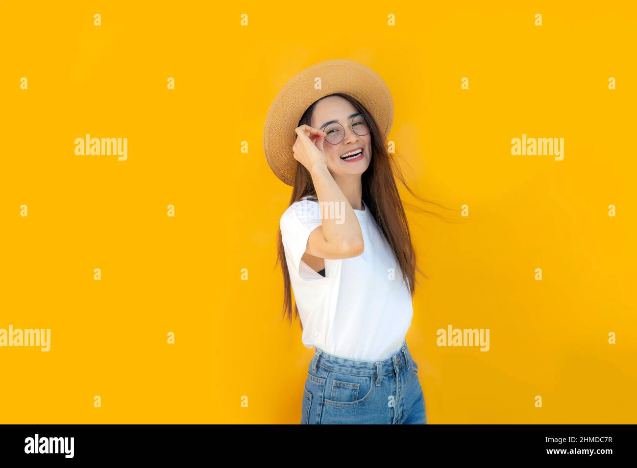 Portrait asian Woman against yellow Background.asian woman wearing glass, rattan hat, white shirt and blue jeans on yellow background for advertising Stock Photo