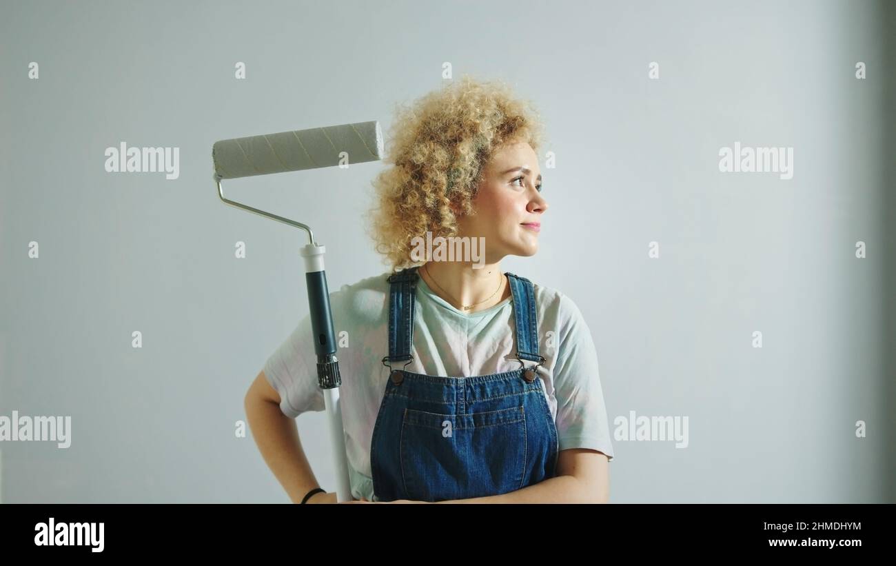 Satisfyied curly hair caucasian with roller paint looking around in freshly panited room. High quality photo Stock Photo