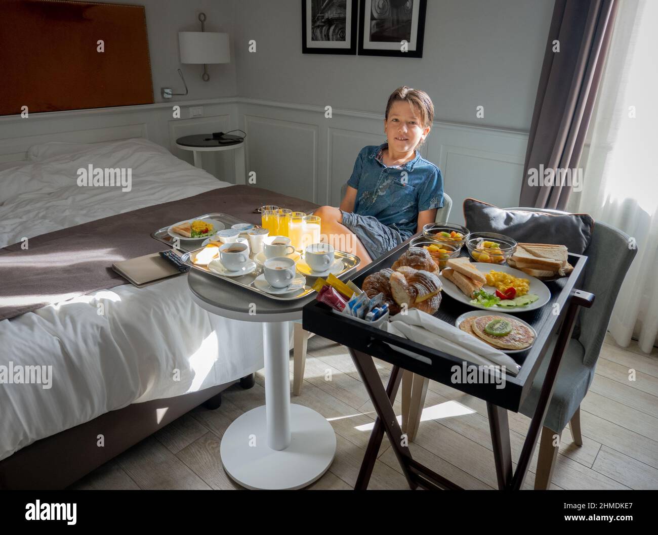 Boy sitting on chair beside freshly various breakfast being served on table in hotel room Stock Photo
