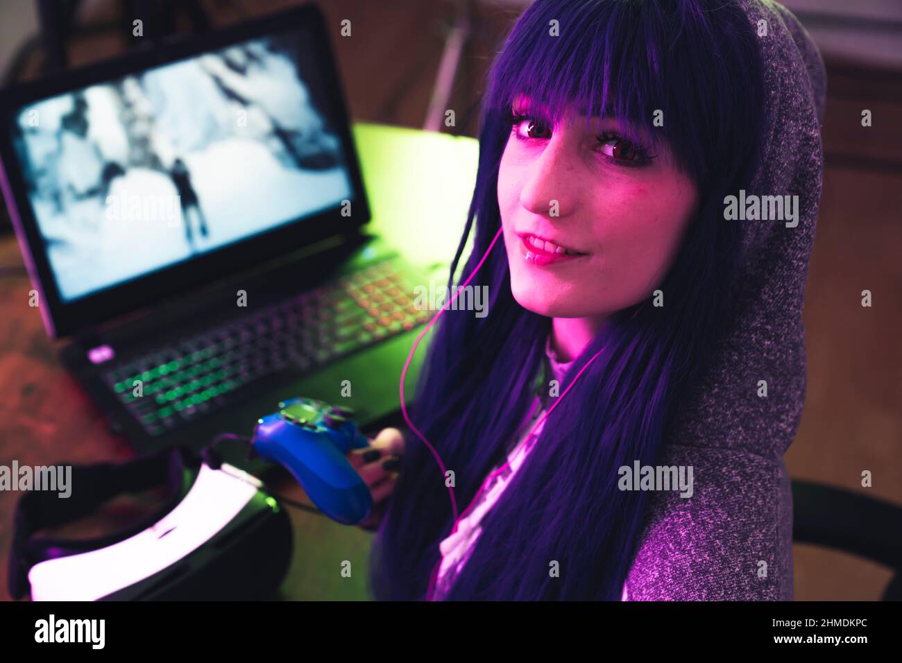 Young brunette in a hoodie uses gamepad and encourages to play with her medium close-up shot. High quality photo Stock Photo