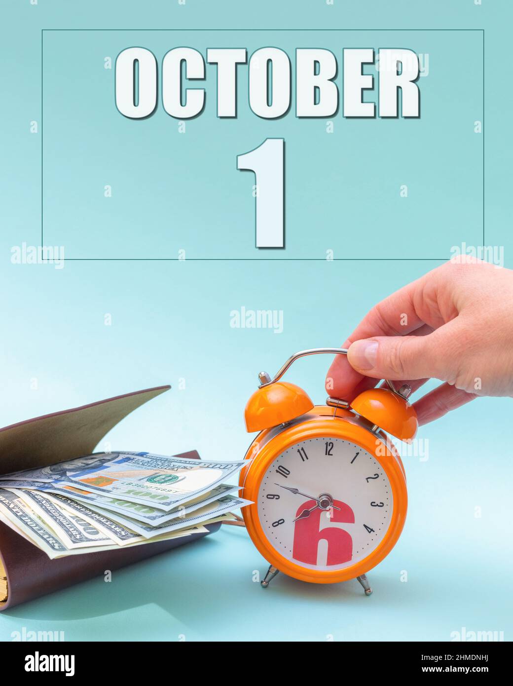 October 1st. Hand holding an orange alarm clock, a wallet with cash and a calendar date. Day 1