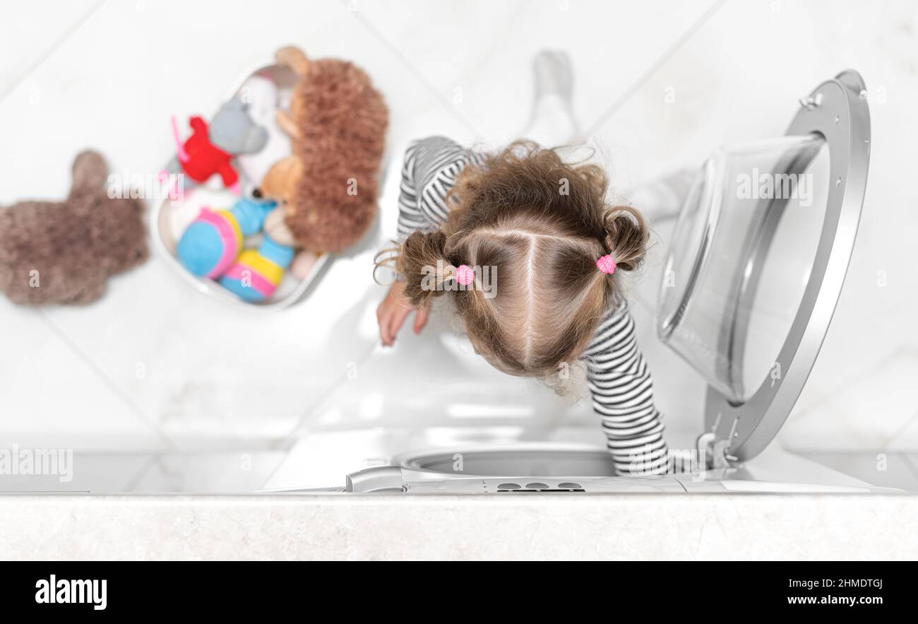 The child puts toys in the washing machine. Stock Photo
