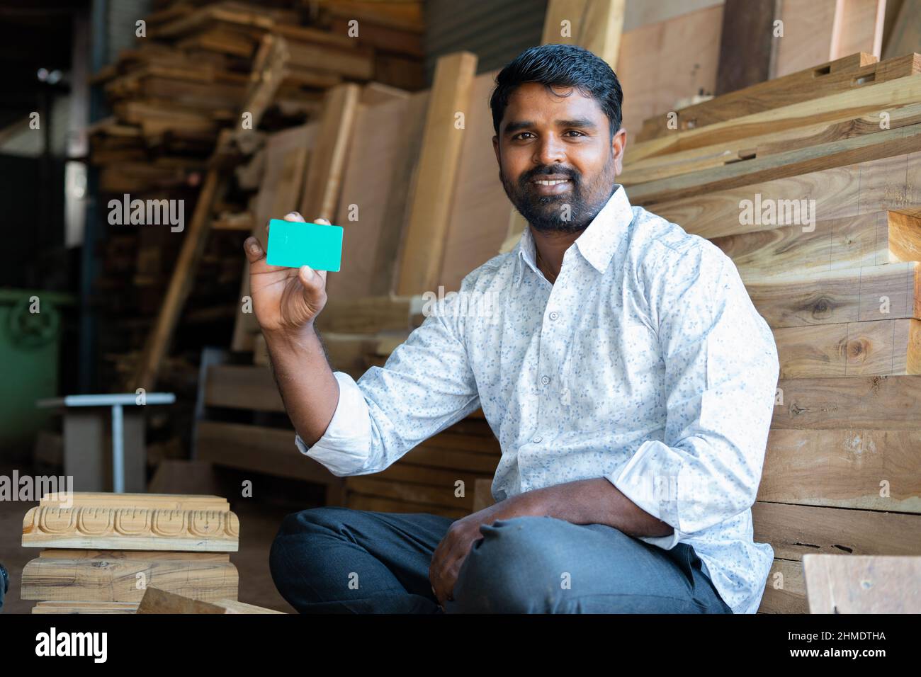 Smiling indian carpenter showing empty green card mockup by looking at