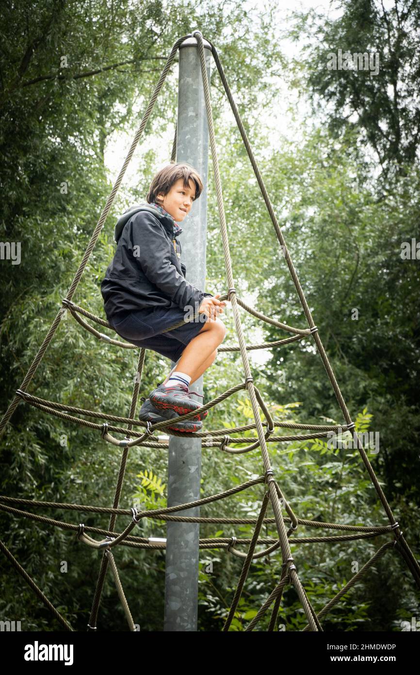 Boy sitting at top of climbing frame in park Stock Photo