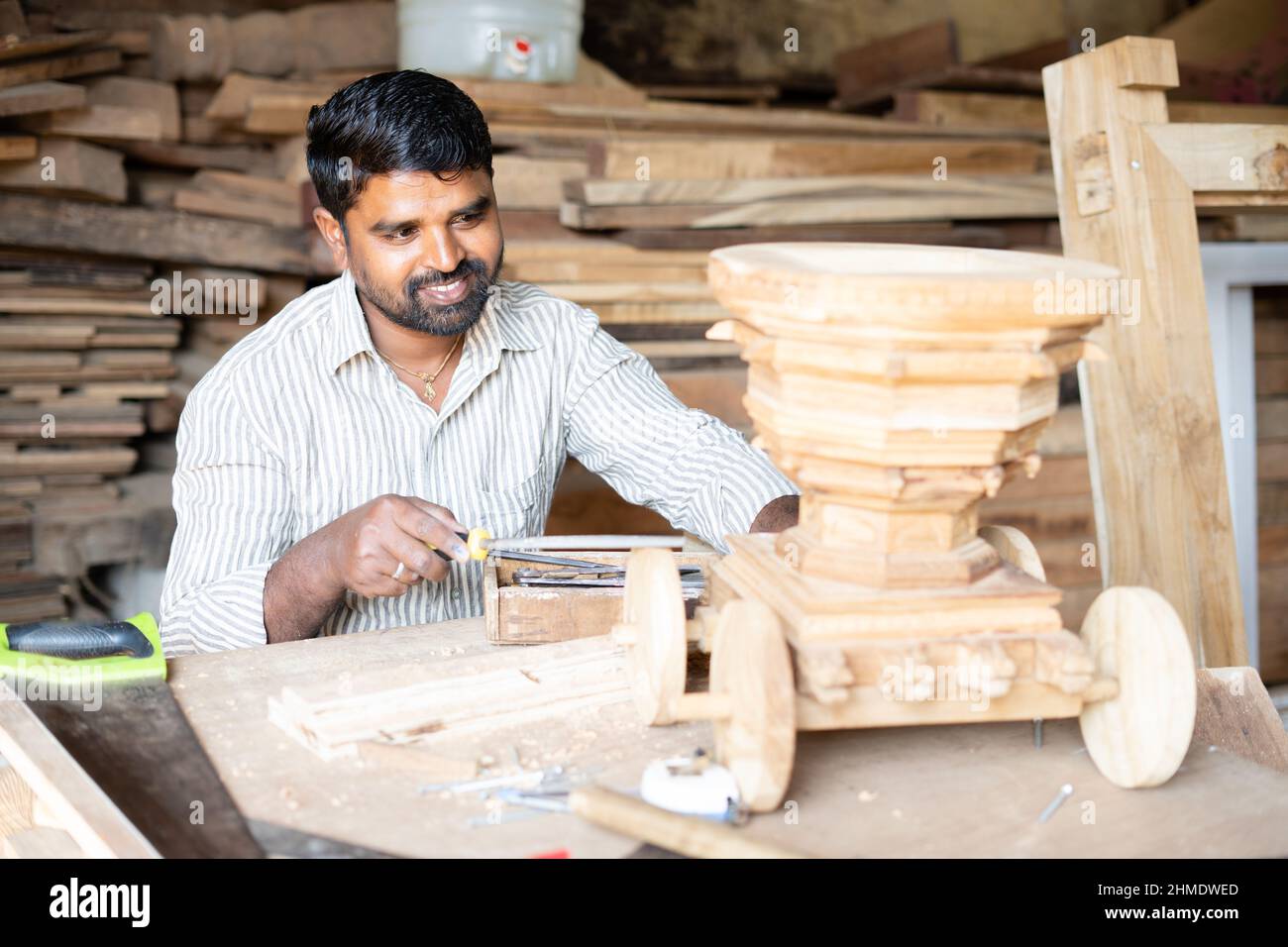 Focus on carpenter, young indian carpenter polising or shaping chariot by using carpentry tools at workplace - concept of craftperson, self employed Stock Photo