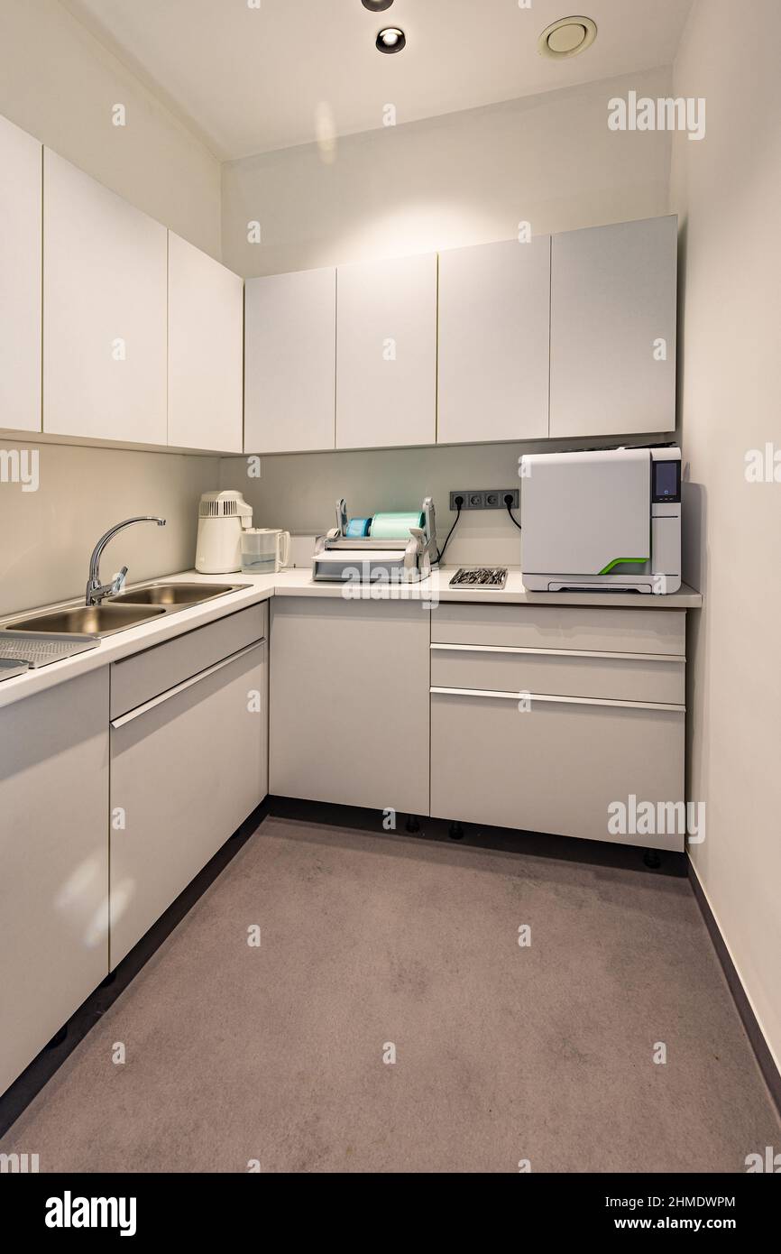 Small room with white walls in a dental clinic. There are light tabletop with a sink, autoclave