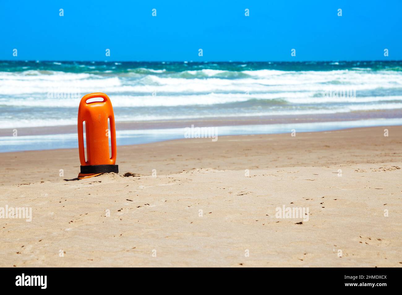 Lifeguard rescue can on the beach. Orange rescue buoy in vertical position on the sand. Stock Photo