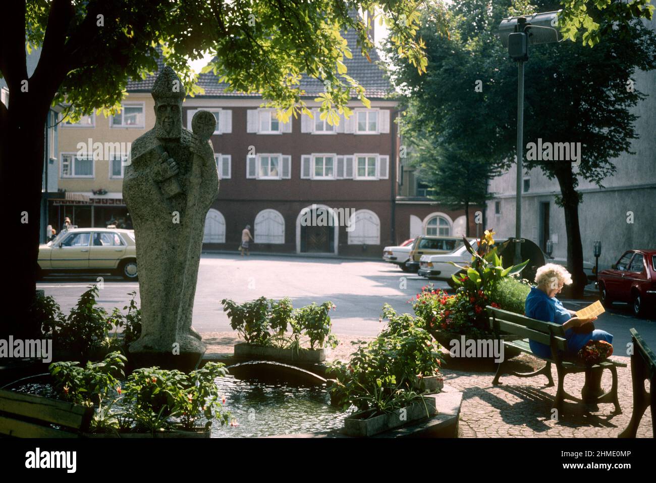 Elderly lady reading on bench beside statue of Bishop Radolf of Verona in 1981, Radolfzell, Baden-Württemberg, Germany Stock Photo