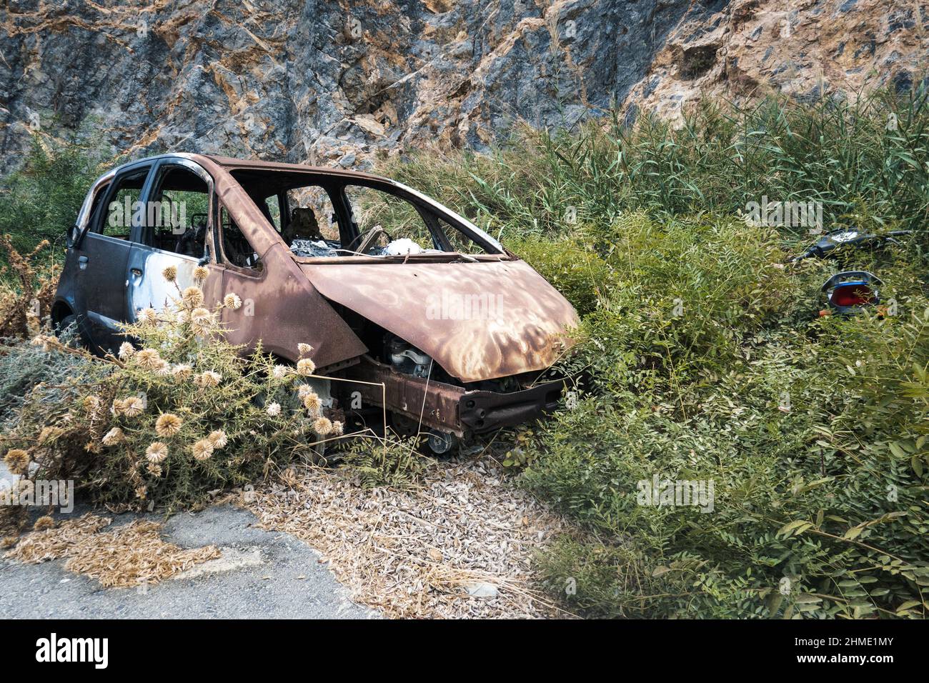 Old broken car surrounded by bushes against rock formations Stock Photo