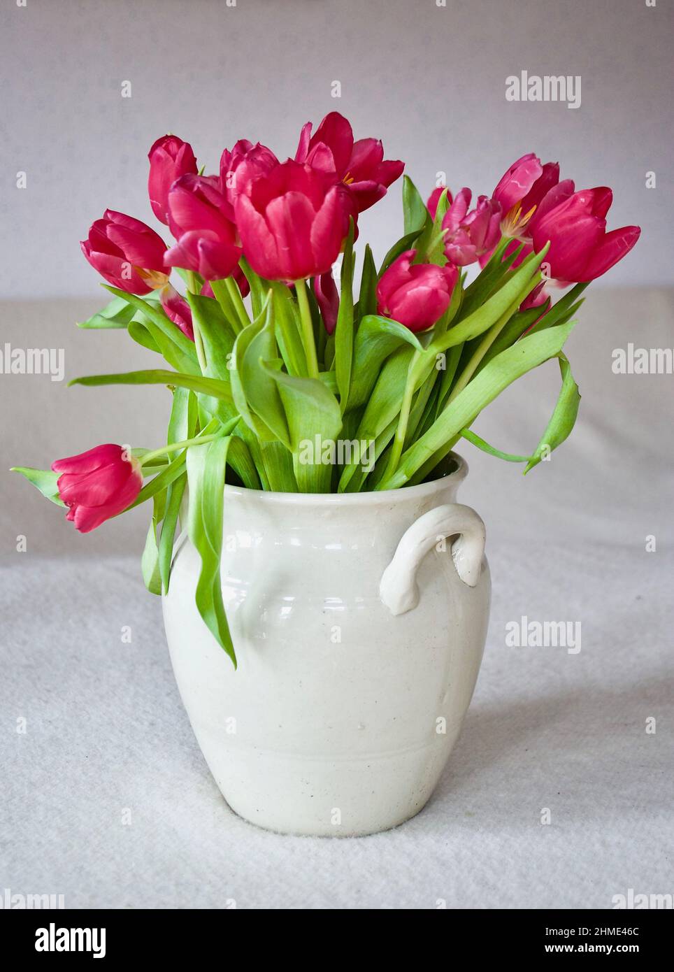 Bouquet with pink tulips in a stoneware pot indoors on a table with ...