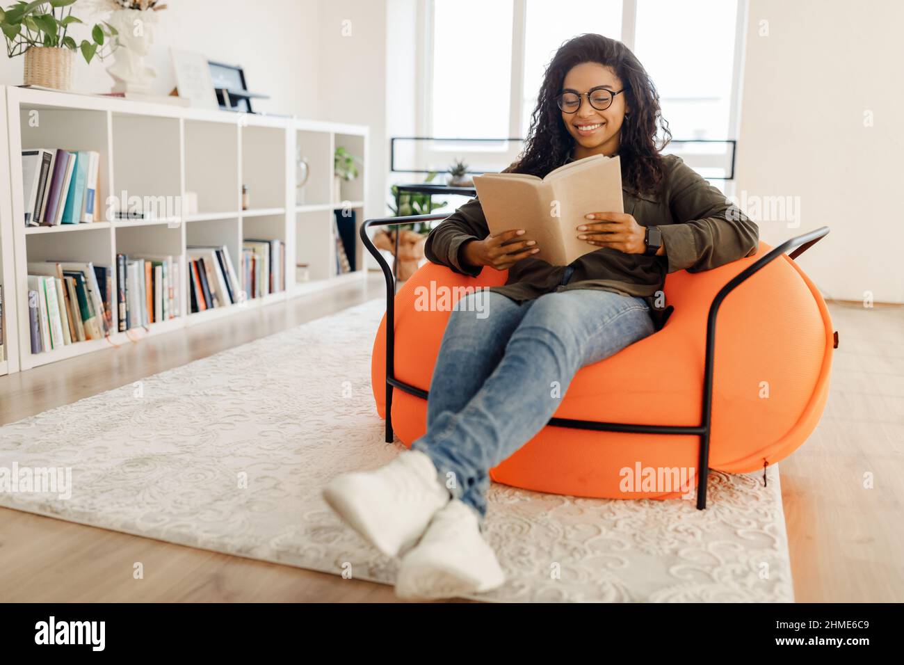 Smiling black woman in eyeglasses reading book Stock Photo